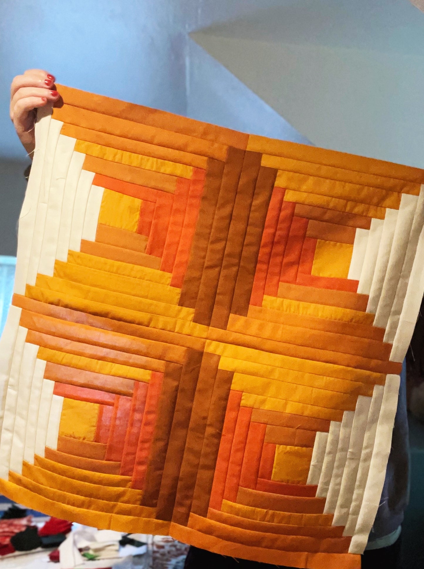 Person holding a quilt with a geometric, log cabin pattern in orange, yellow, and white.
