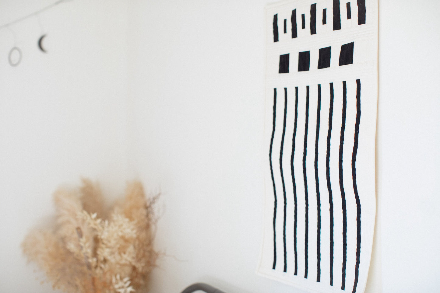 A view of a modern black and white quilt made of squares and stripes hanging on a wall in a minimalist room.