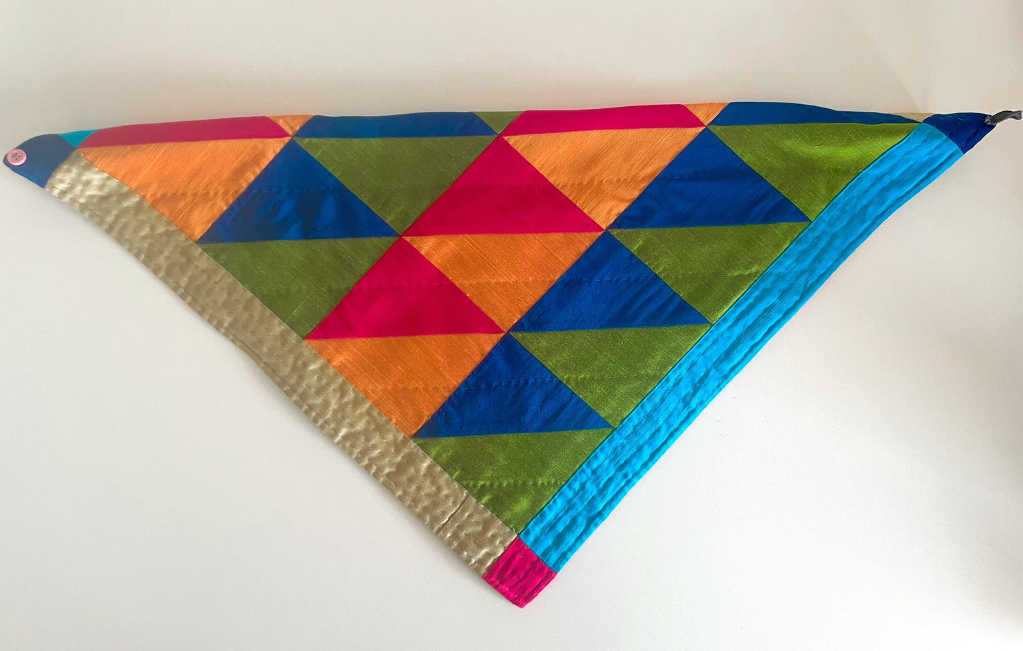 A quilted bandana of triangles in pink orange blue and green lays folded on the table. 