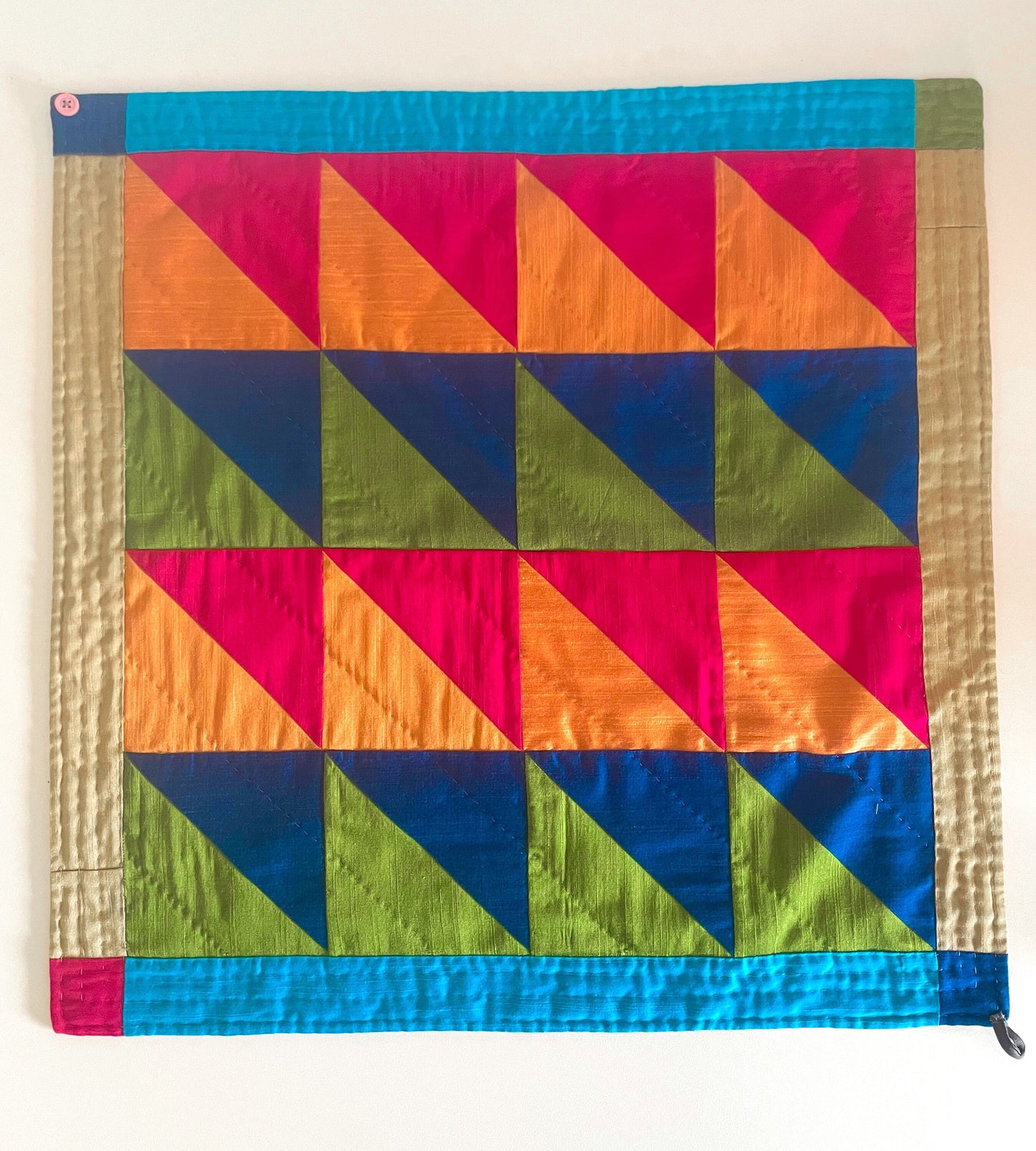 A quilted bandana lays on the table. The design is triangles in pinks, oranges, green and blues. 