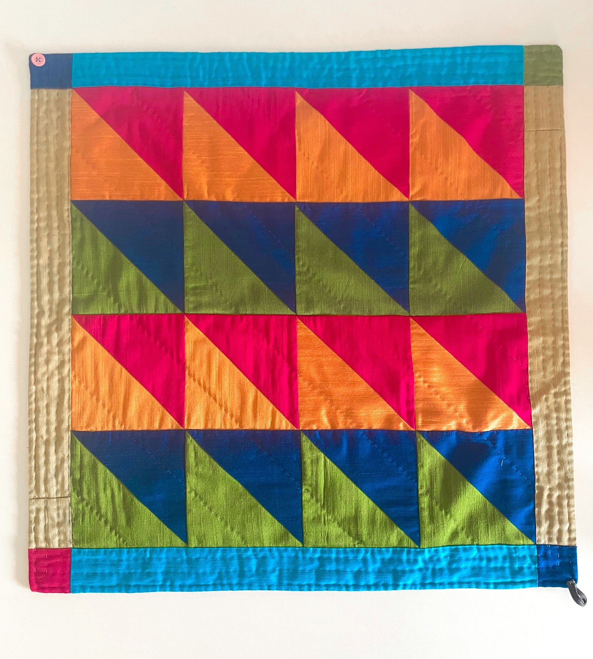 A quilted bandana lays on the table. The design is triangles in pinks, oranges, green and blues. 