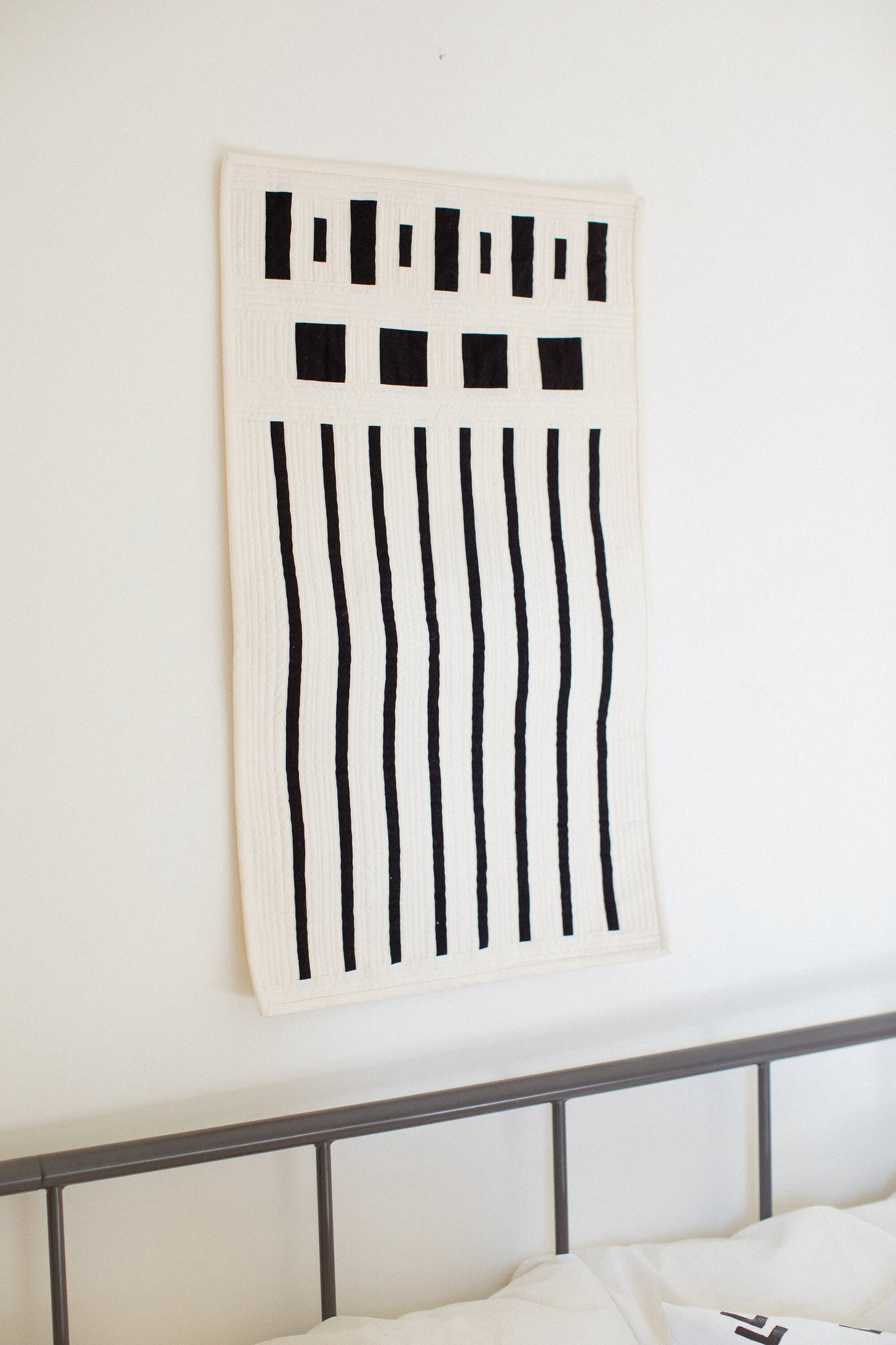 Side view of a modern minimalist quilt with a bed in the background. 