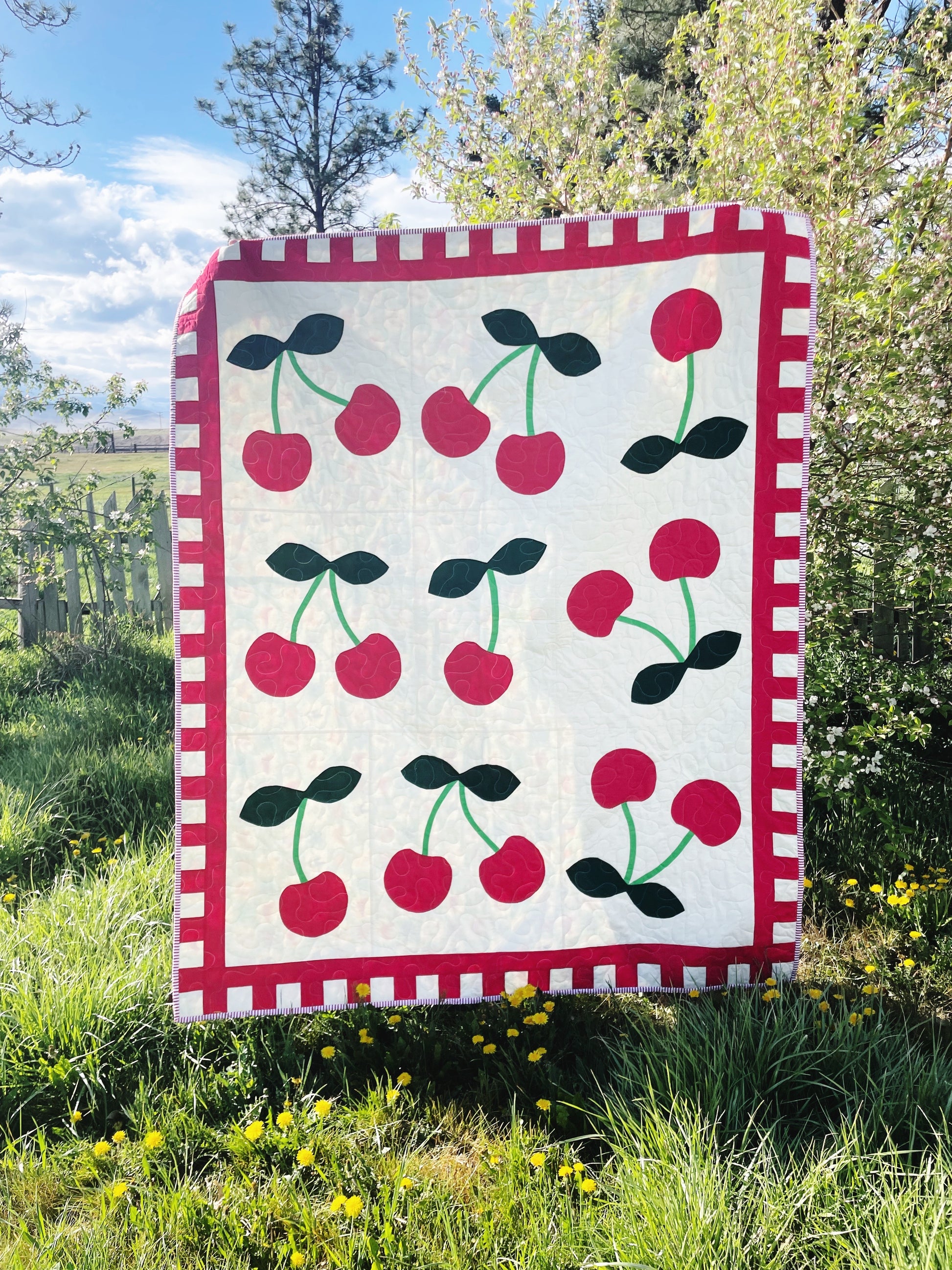 A quilt pattern featuring a repeated design of oversized cherries with green leaves on a white background, bordered with a red and white striped pattern.