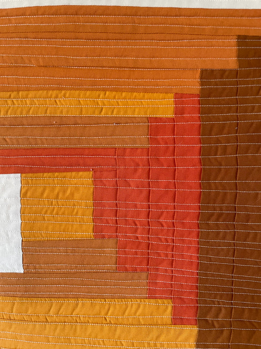 Quilt with a patchwork design featuring shades of brown, orange, and red.