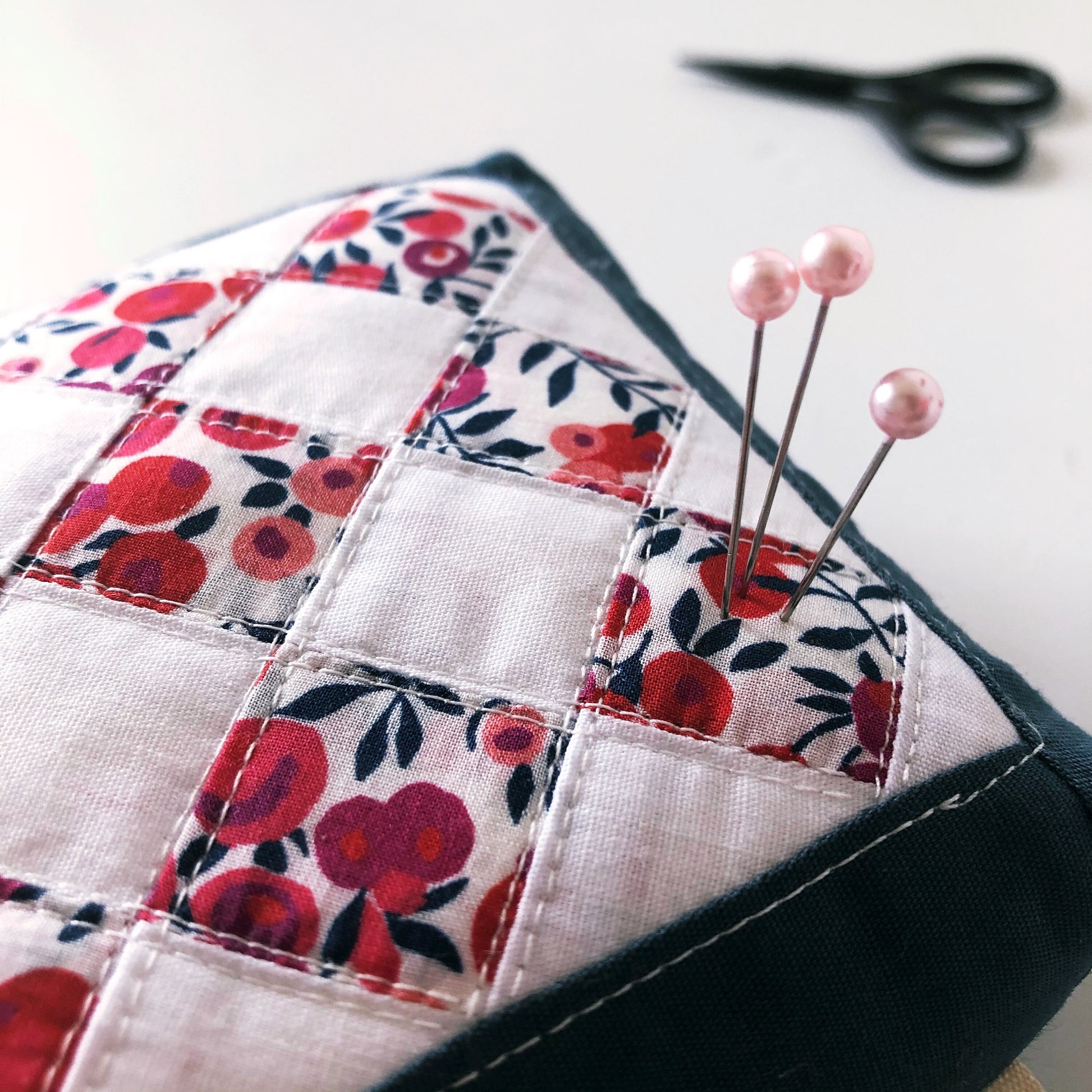 A closeup of a pincushion made from red and blue scraps with pins in it. 