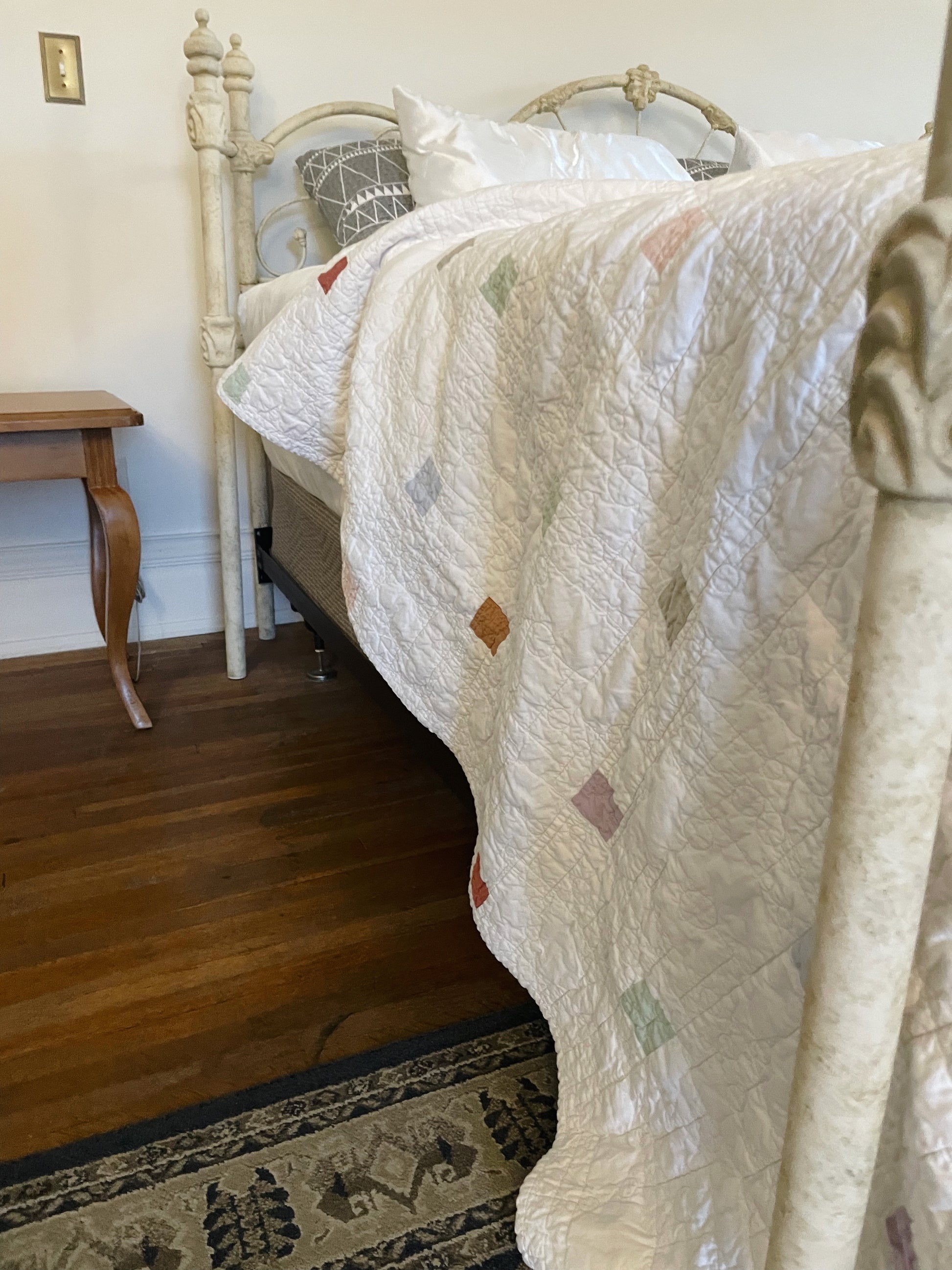 Bed with a patterned quilt draped over the foot of the bed in a bedroom setting.