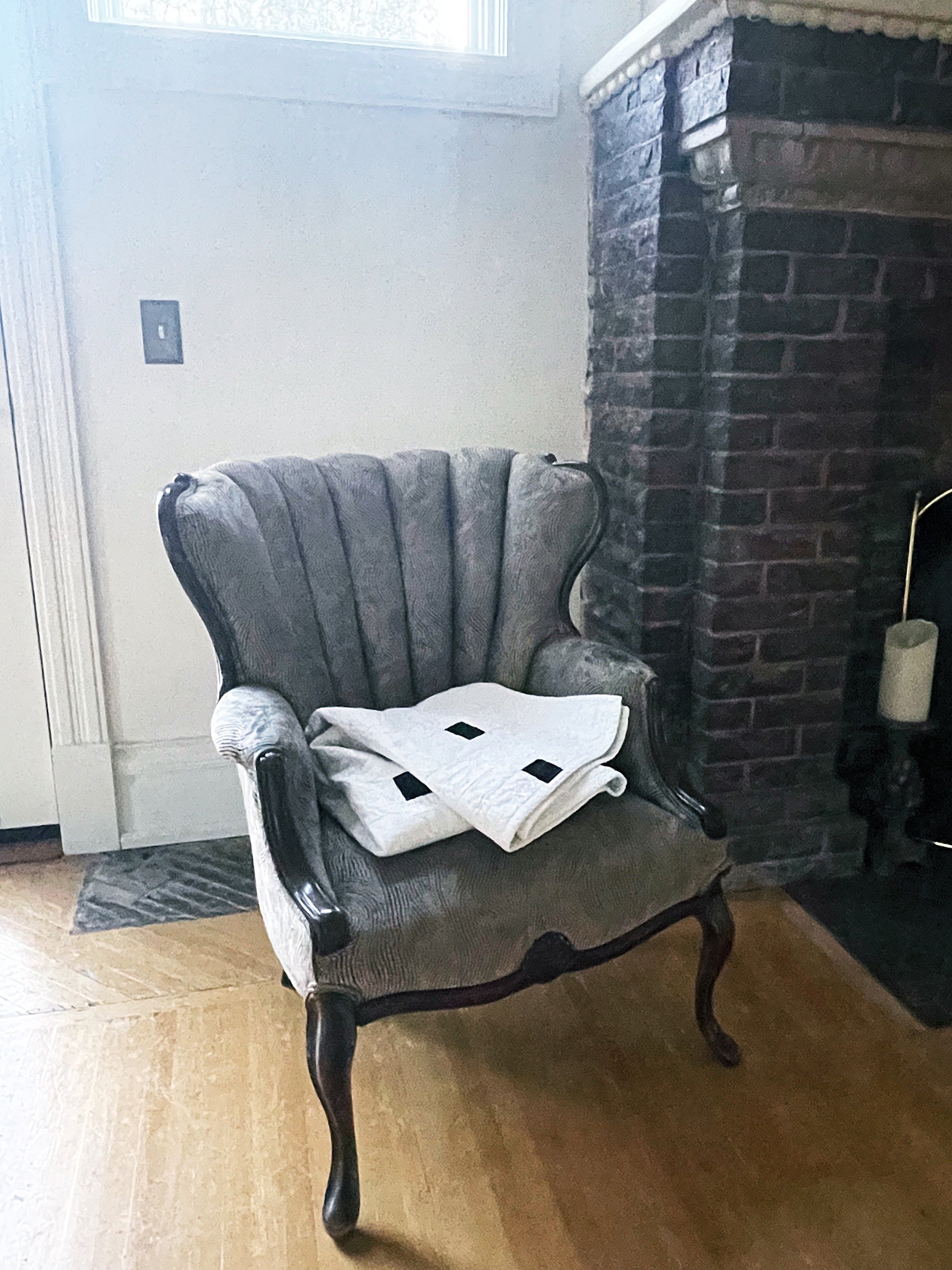 Gray armchair with a white quilt in front of a brick fireplace.