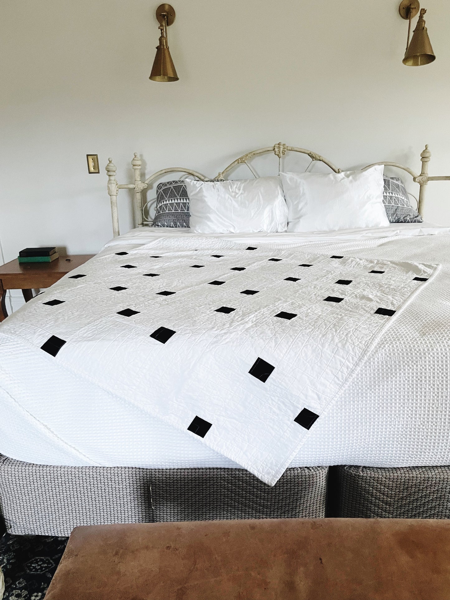 Bed with a white quilt featuring black diamond patterns, in a bedroom setting.