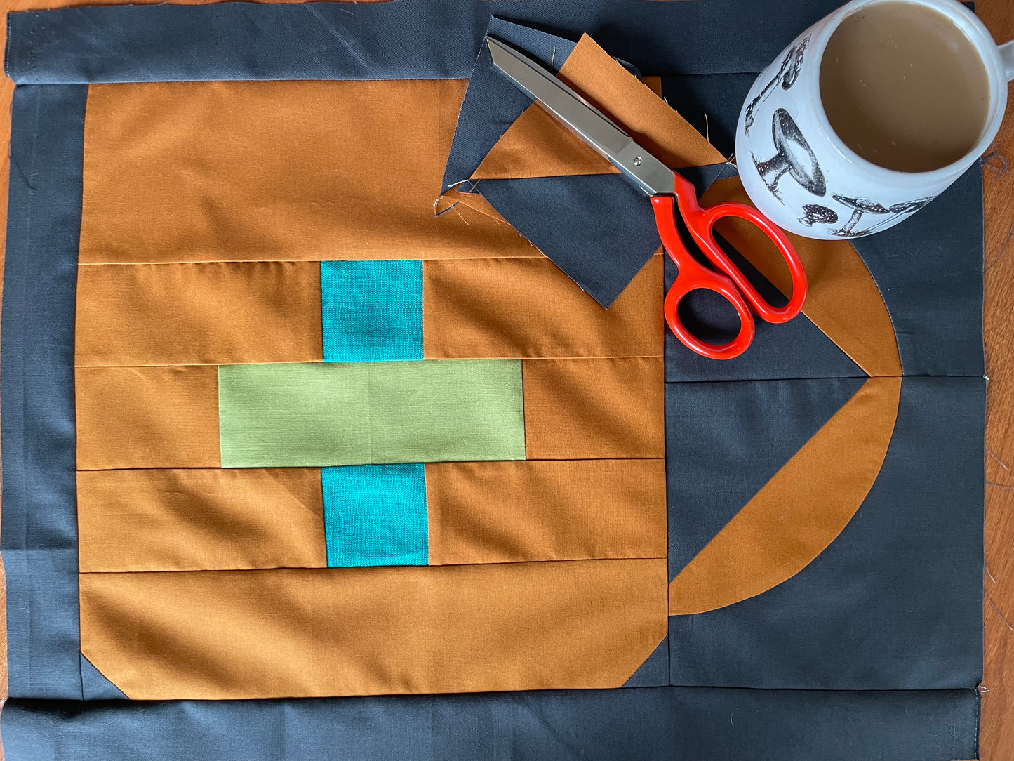 Fabric with cut-out shapes, scissors, and a mug on a wooden surface