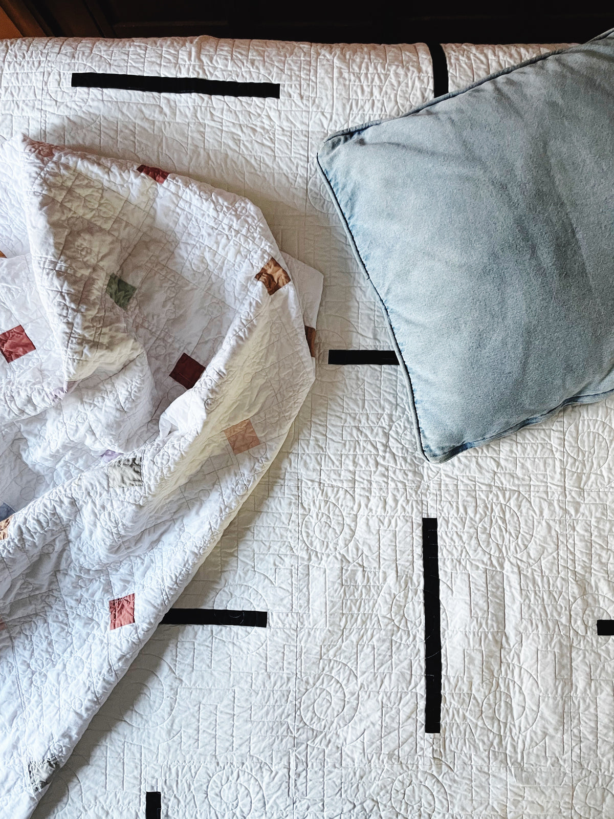 A warm white quilt with textured pattern on a bed, featuring a faded blue, denim pillow.