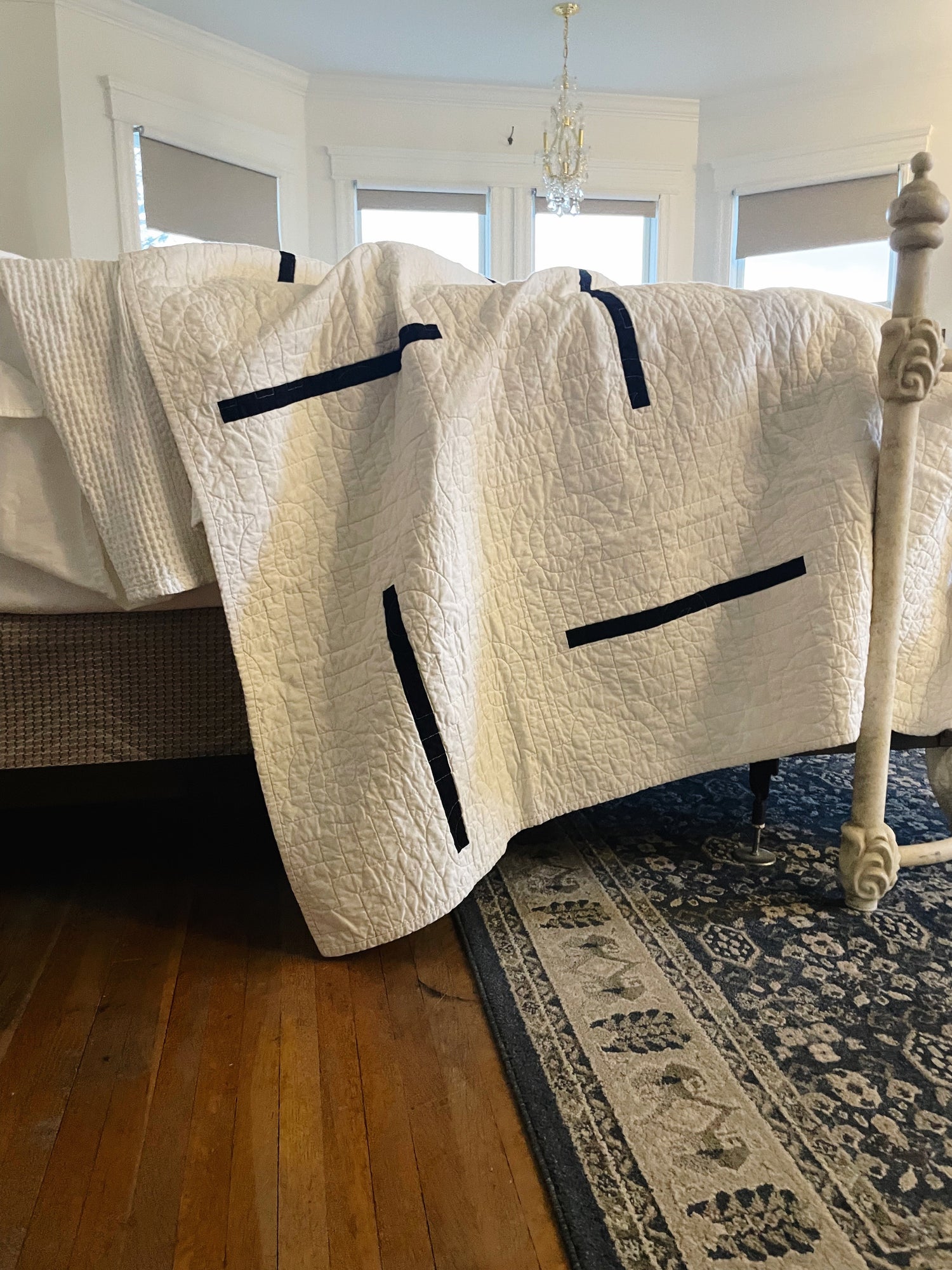 White quilt with black accents on a bed in a bedroom with wooden floor and rug.