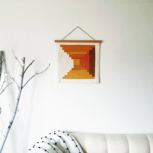Hanging quilted wall art with geometric, log cabin pattern on a white wall.