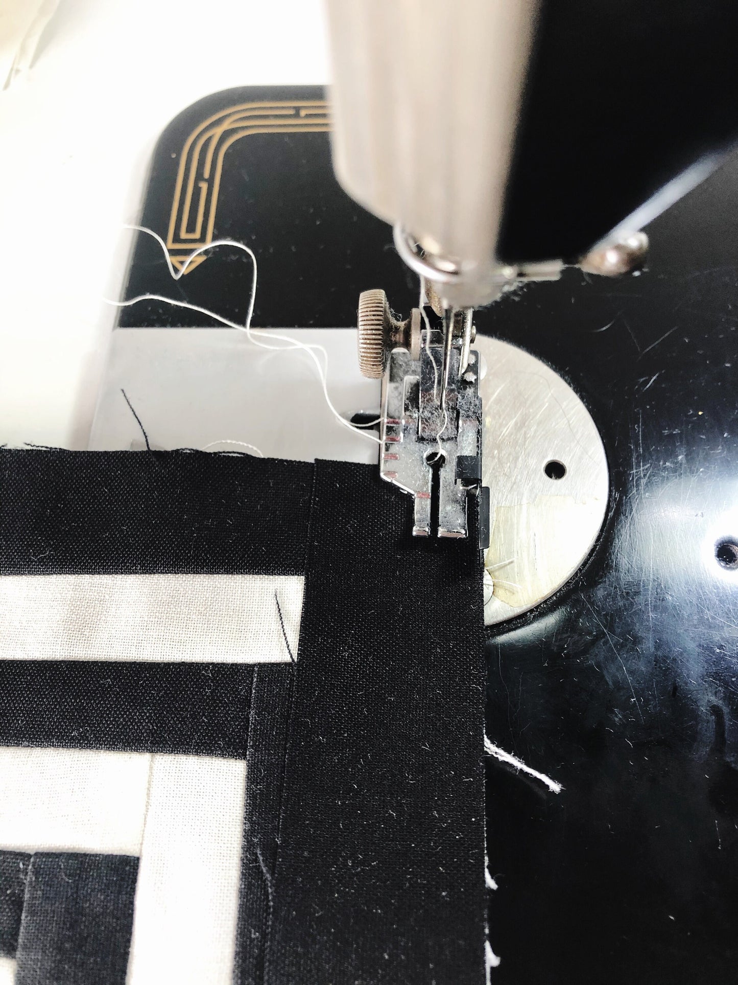 A closeup view of a quarter inch pressor foot. it's sitting at the beginning of a seam ready to sew together black and white fabric. 