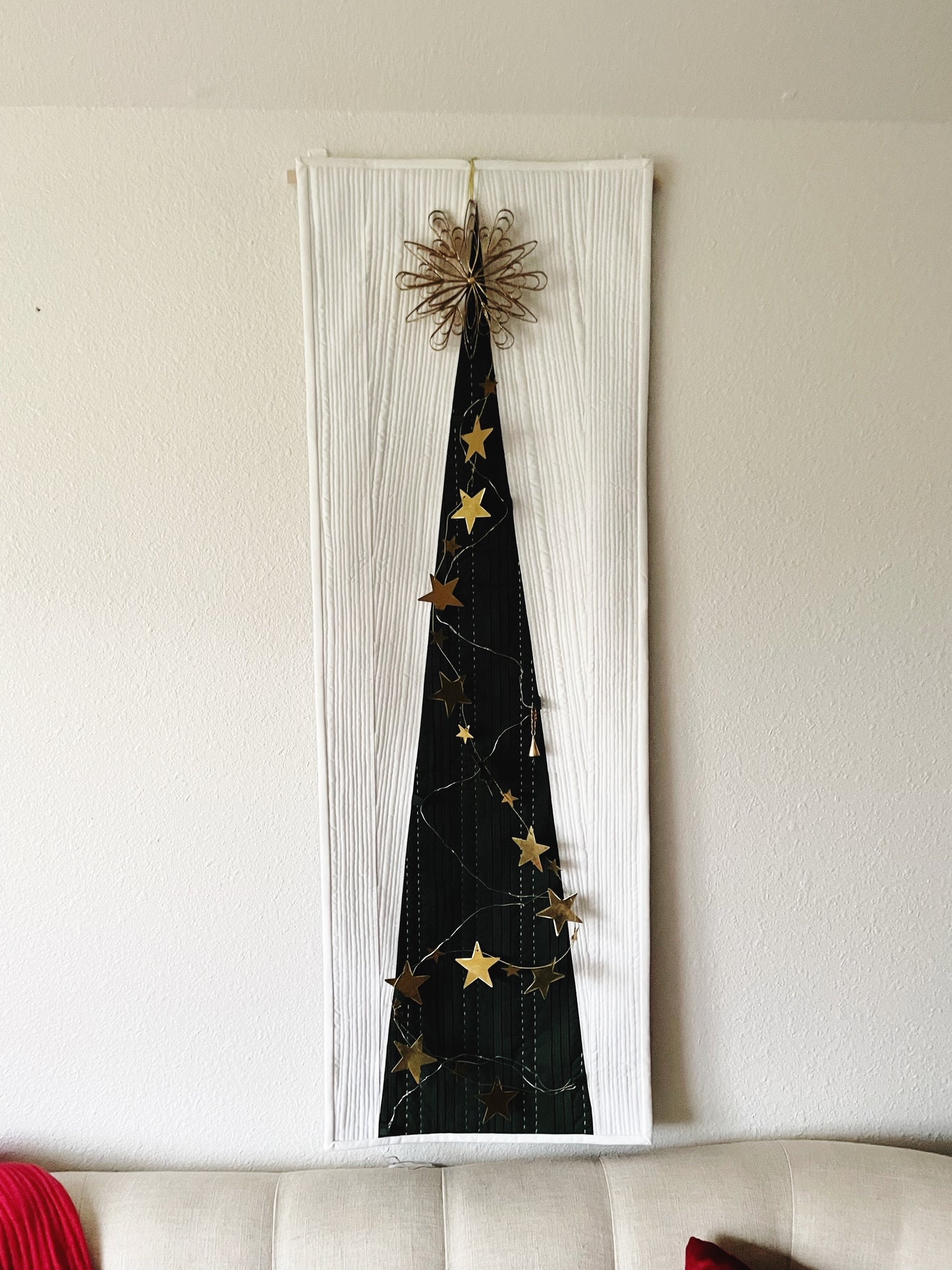 Decorative wall art with a green quilted tree shape and gold stars on a white background