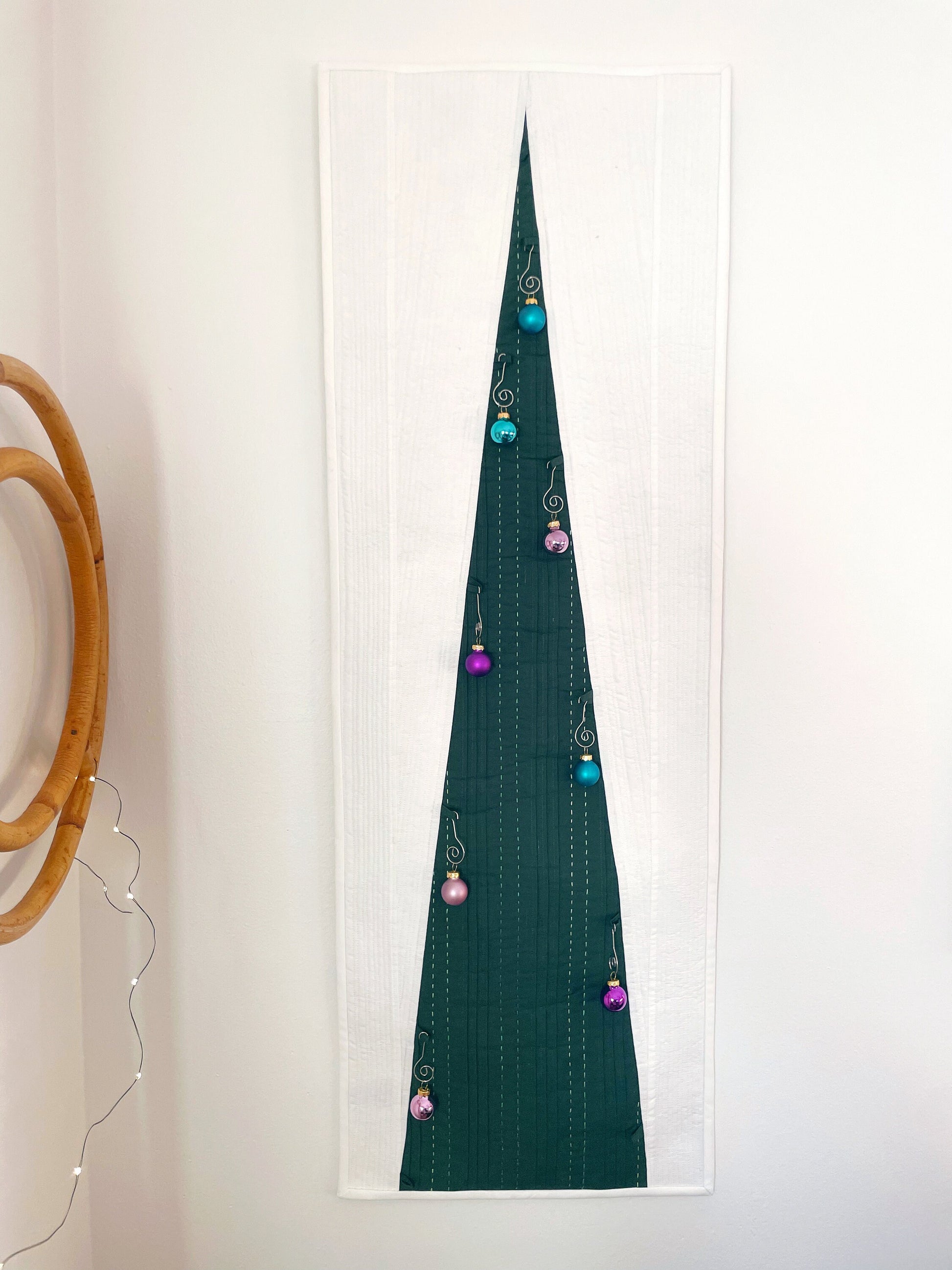 A quilted wall hanging in the shape of a Christmas tree with geometric patterns and holiday ornaments.