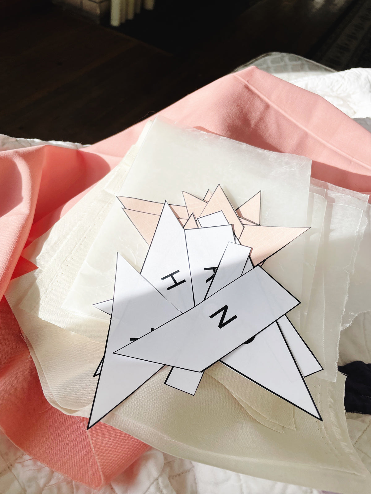 White paper with geometric shapes and letters on a pink fabric background