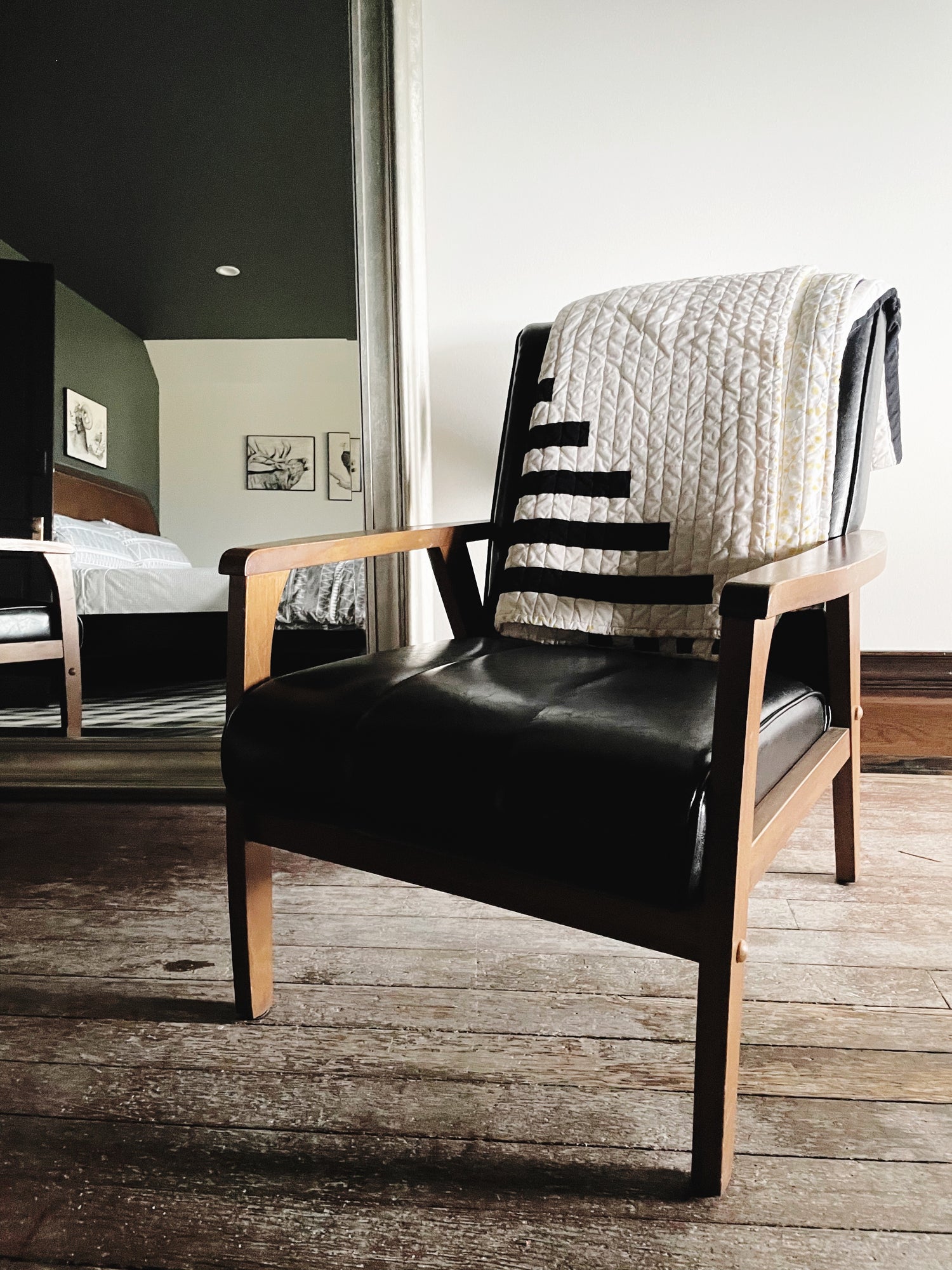 black and white quilt folded on black leather chair with wooden frame on a wooden floor, room in the background mirror