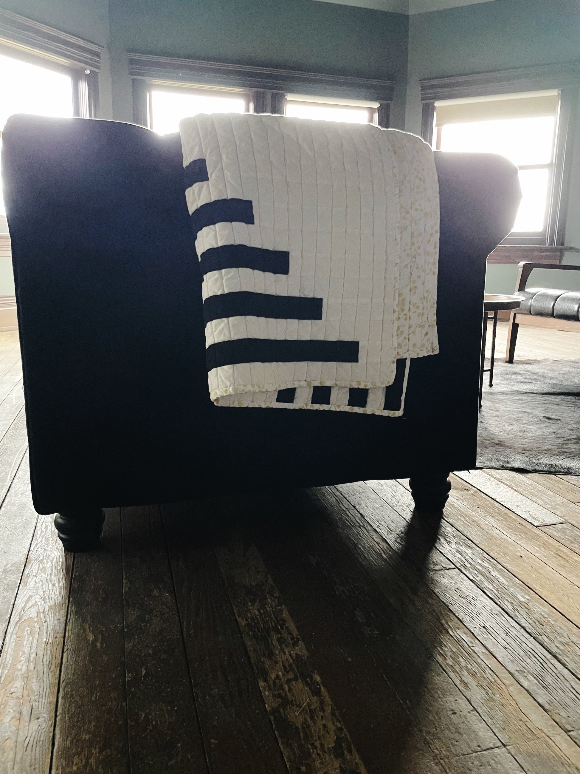 A black and white modern quilt is folded over a black couch.