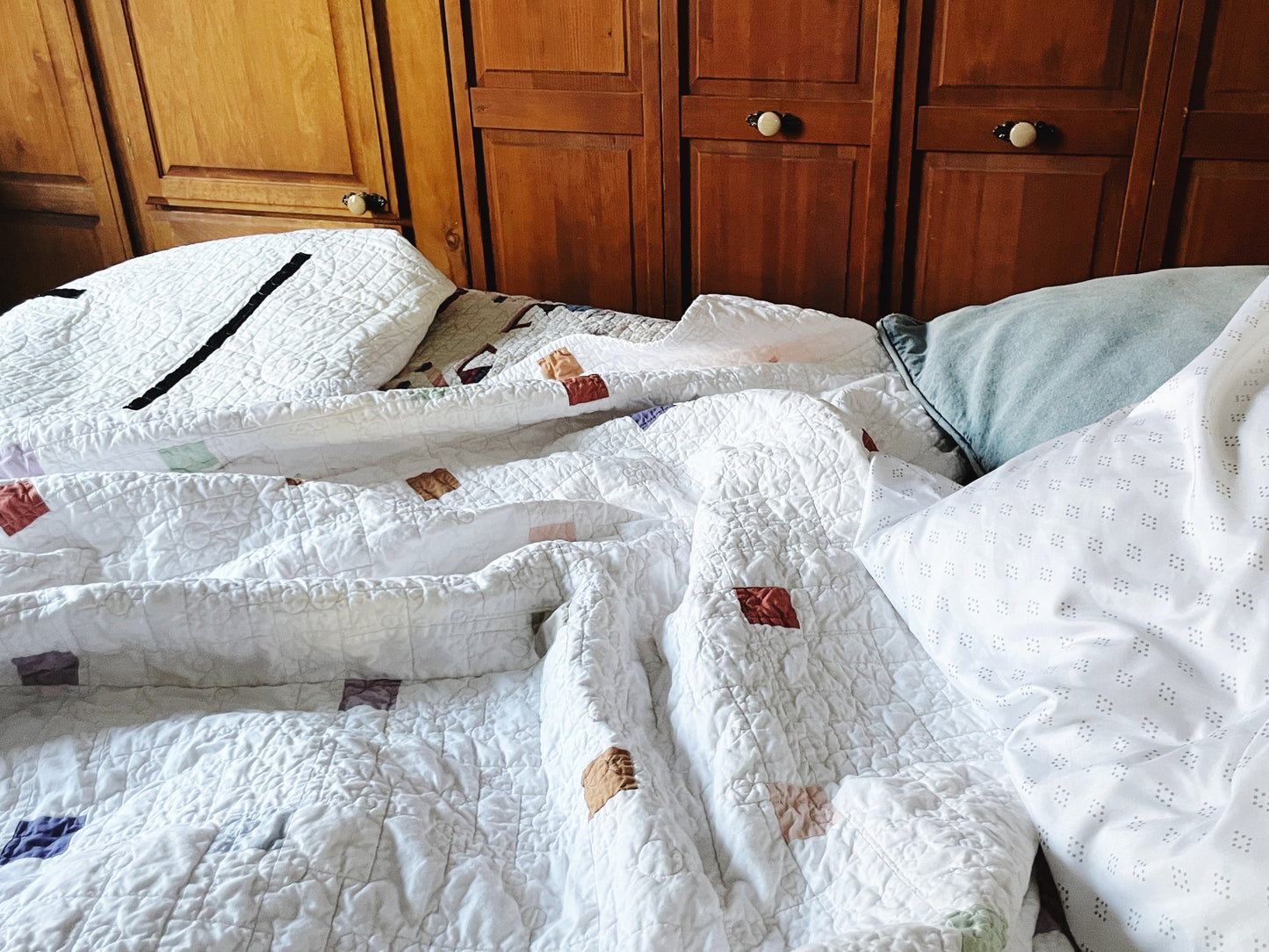 Bed with modern, minimalist quilts and pillows in front of wooden cabinets