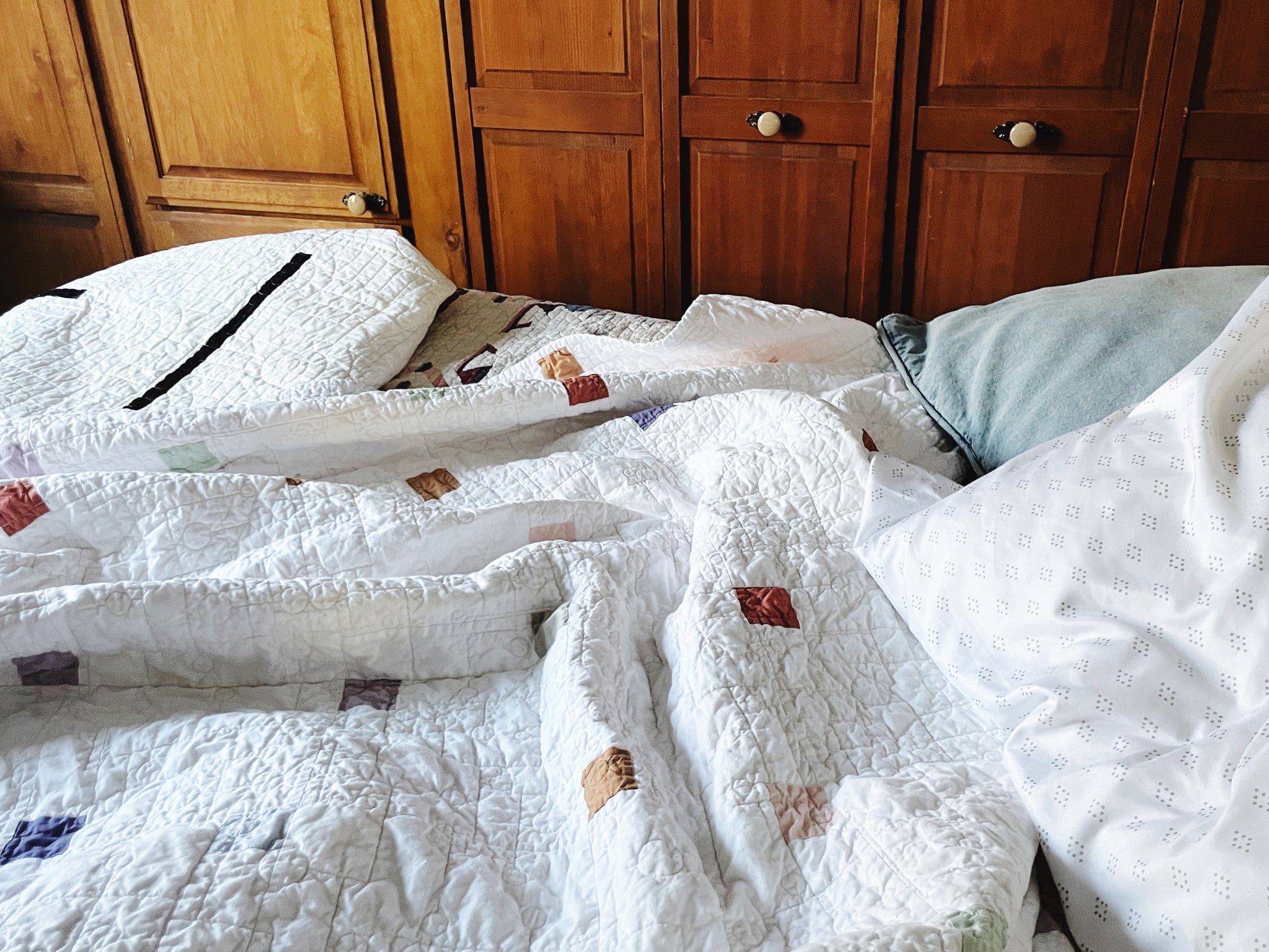 Bed with modern, minimalist quilts and pillows in front of wooden cabinets