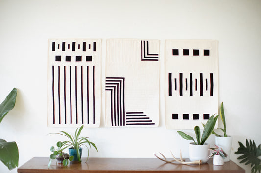 A straight view of modern quilts hanging on a wall above a sideboard with plants and antlers