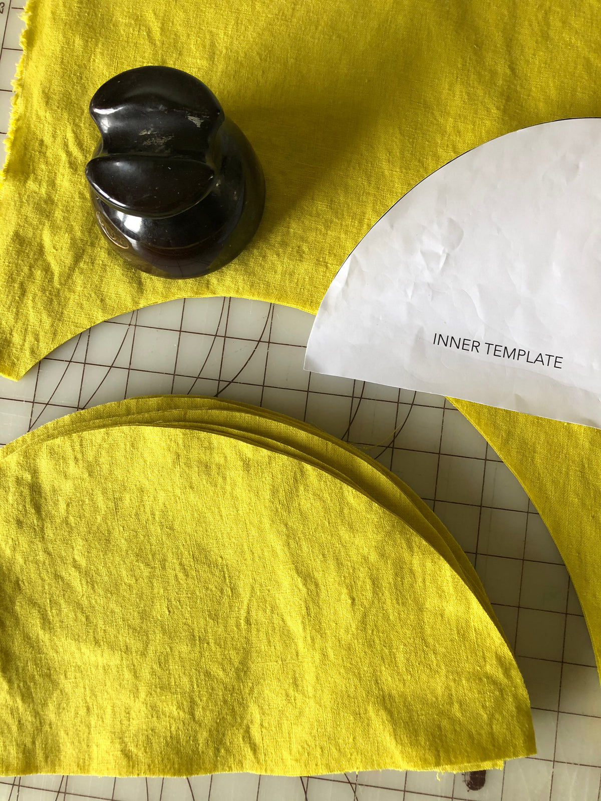 A top down view of yellow curved quilt blocks being cut using a paper template. 