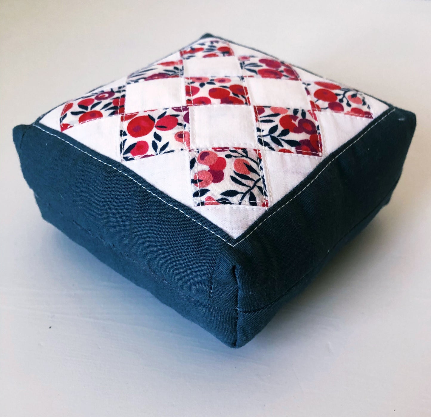 A pincushion with red and blue fabric on a white background in a design using small squares. 