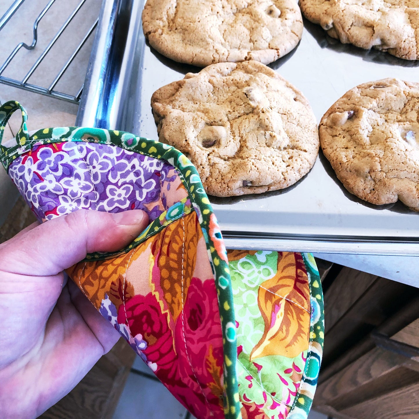 A hand shown holding a colorful quilted pot holder holding a tray of freshly baked bookies. 