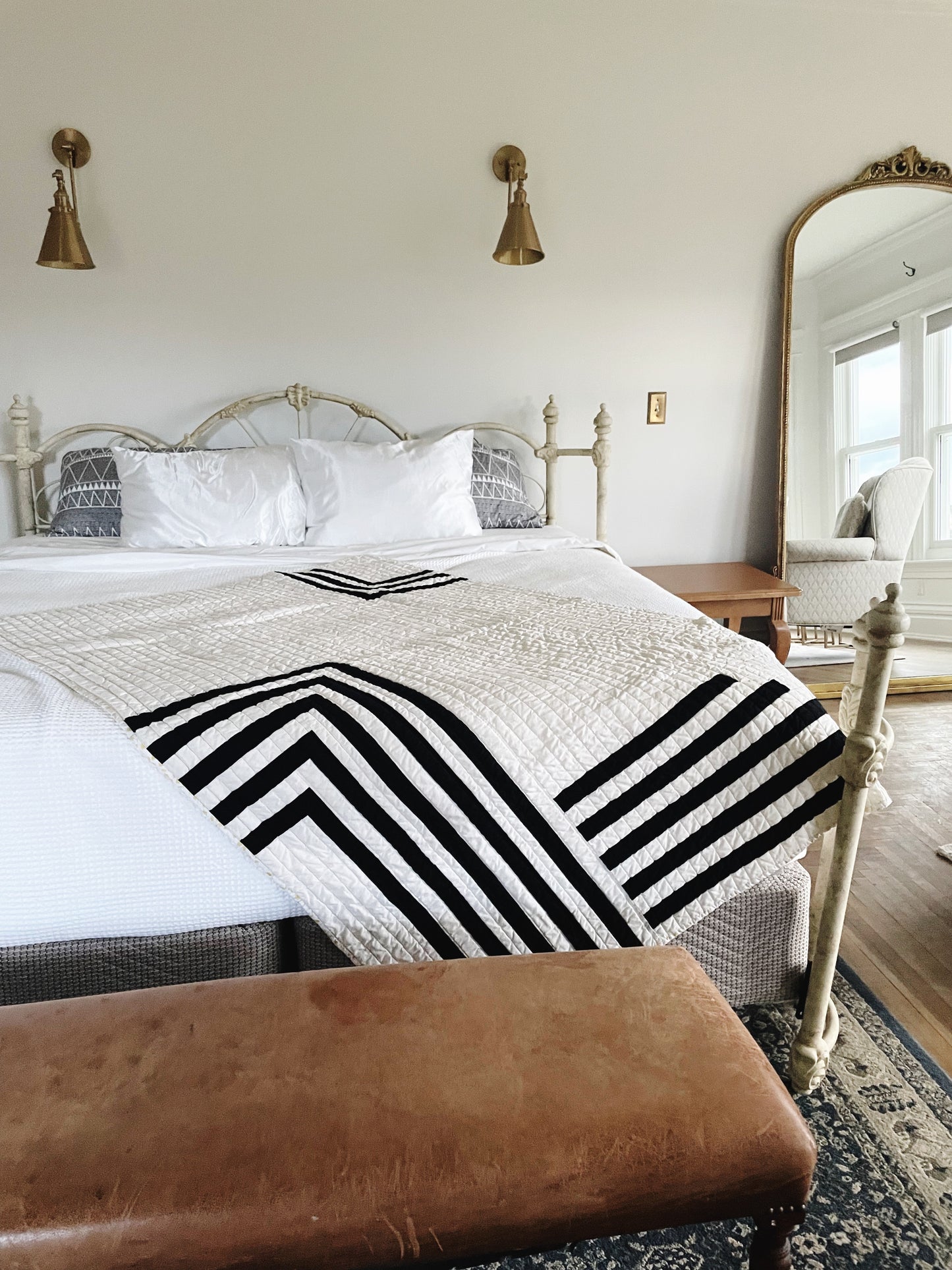 Bedroom with a bed featuring a black and white striped blanket, a brown bench, and wall sconces.